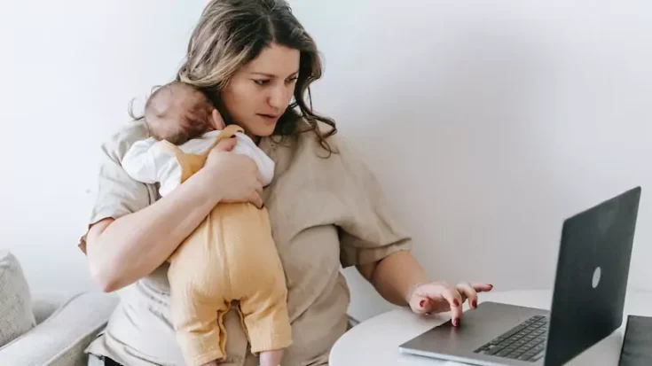 Woman cuddling baby and using laptop