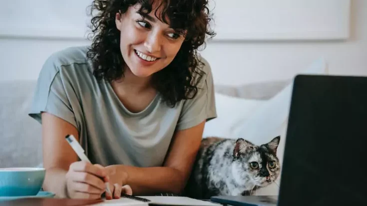 Woman with cat writing in planner while using laptop